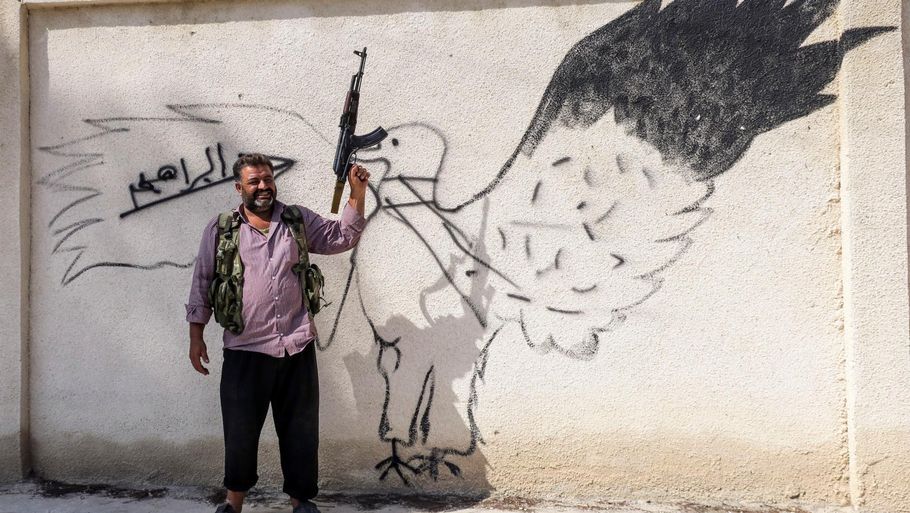 En kriger står foran en væg med grafitti, efter den frie syriske hær har fordrevet IS fra byen Jarablus. Foto: AP