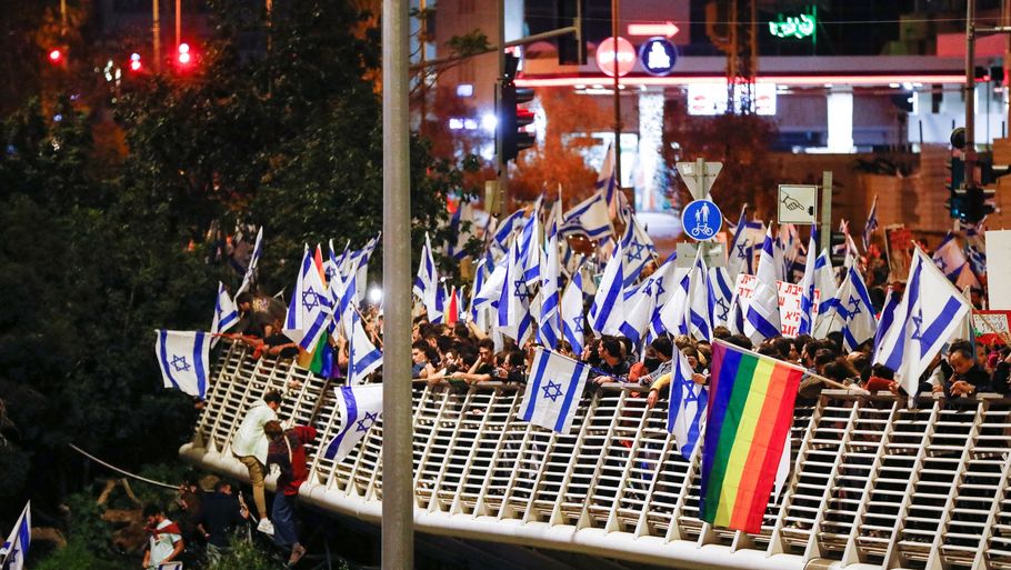 En skov af israelske flag - og et enkelt regnbueflag - vajer over den vigtigste hovedvej ind til Tel Aviv, som demonstranter blokerer lørdag aften i protest mod de ændringer, Netanyahus regering vil gennemføre inden for retssystemet. I flere byer er der efter alt at dømme rekordmange deltagere. Foto: Nir Elias/Reuters