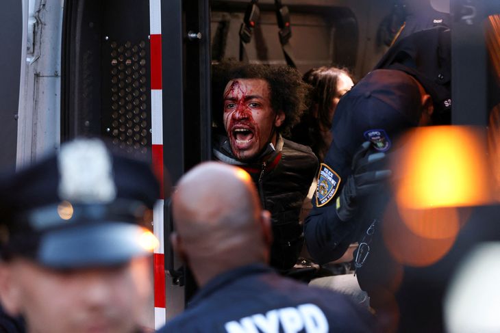 En mand med falsk blod malet i ansigtet bliver ført væk af politiet. Foto: Andrew Kelly/Ritzau Scanpix